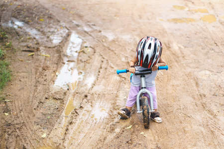 Asian boy about 1 year and 6 months is playing with baby balance bike on muddy road at rural countrysideの写真素材