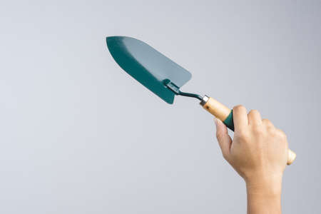 Hand holding green garden shovel with wooden handle on white backgroundの写真素材