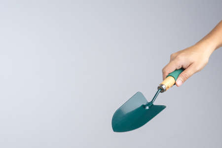 Hand holding green garden shovel with wooden handle on white backgroundの写真素材