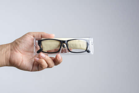 Hand holding plastic case box with clean dust cloth and a pair of black plastic prescription optical glasses on white backgroundの写真素材