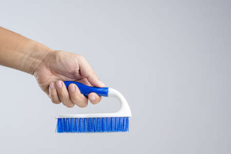 Hand holding new blue floor brush with plastic handle on white background