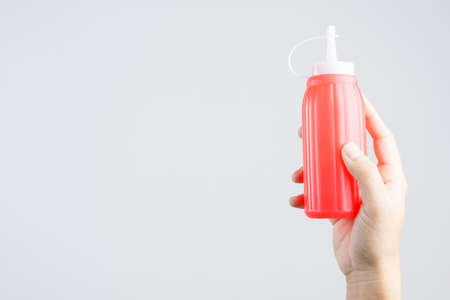 Hand holding red sauce bottle for ketchup or hot chili pepper on white backgroundの写真素材