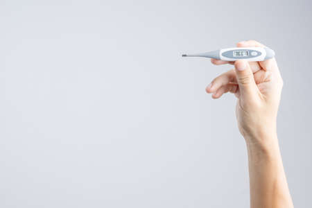 Hand holding electronic digital thermometer with healthy human body temperature at 36.6 degrees celsius on display on white backgroundの写真素材