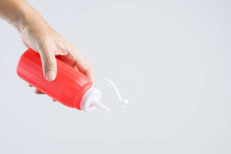 Hand holding red sauce bottle for ketchup or hot chili pepper on white backgroundの写真素材