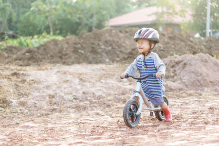 Asian boy about 1 year and 9 months is riding  baby balance bike on muddy construction road at rural countrysideの写真素材