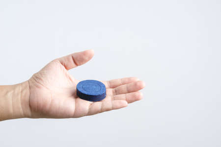 Hand holding automatic Bleach toilet bowl cleaner stain remover blue tab or tablet flush tank on...