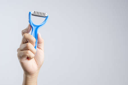 Hand holding plastic fruit peeler with blue handle on white backgroundの写真素材
