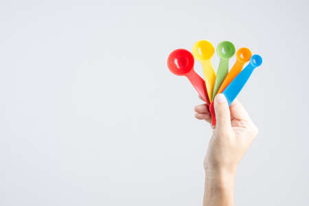 Hand holding set of measuring spoons made of colored plastic on white backgroundの写真素材