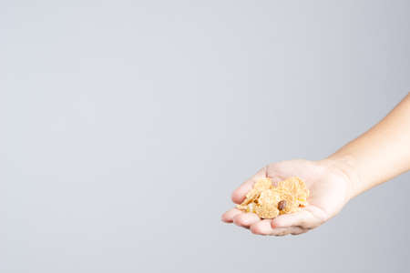 Hand with crispy whole wheat grain cereal, with mixing dry fruits from pineapple, papaya and raisin on white backgroundの写真素材