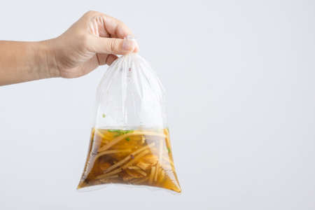 Hand holding boiled braised fish maw in red gravy with blood soup, peppers in plastic bag wrapped by rubber band, A Thai Chinese food on white backgroundの写真素材