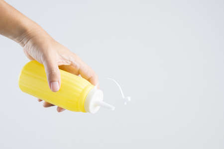 Hand holding yellow sauce bottle for mayonnaise or mustard on white backgroundの写真素材