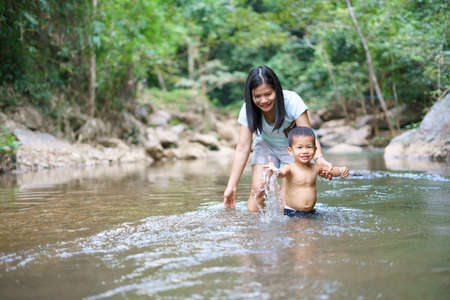 Asian mother in blue shirt with DIY chest pocket playing water with her son about 1 year and 9...