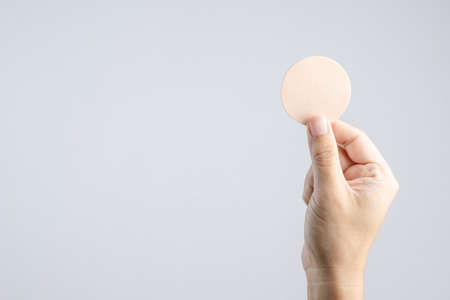 Hand holding round brown face sponge for cosmetic on white background