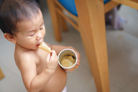 A year and three months old Asian baby eating fried potato chip by himself