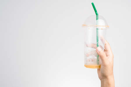 Hand holding empty plastic cup of Thai milk ice tea with green straw on white backgroundの写真素材