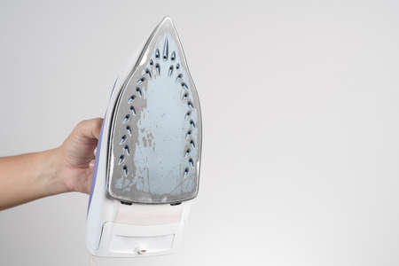 Hand holding old and damage electric clothes iron on white backgroundの写真素材