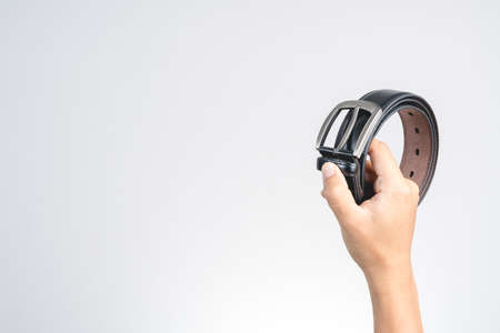 Hand holding old style or retro black leather belt with metal head on white background