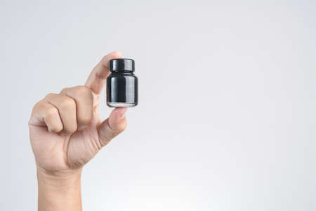 Hand holding black ink or acrylic color bottle on white backgroundの写真素材