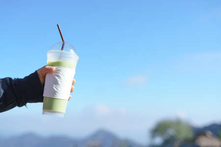 hand holding iced green tea cup on blue sky backgroundの写真素材