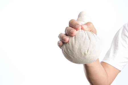 hand holding thai herbal compress ball for massage therapy on white backgroundの写真素材