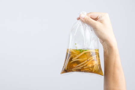 Hand holding boiled braised fish maw in red gravy with blood soup, peppers in plastic bag wrapped by rubber band, A Thai Chinese food on white backgroundの写真素材