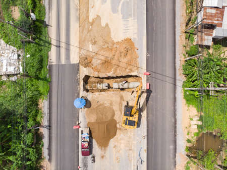 Water pipe excavator job by backhoe and workers near road construction siteの写真素材