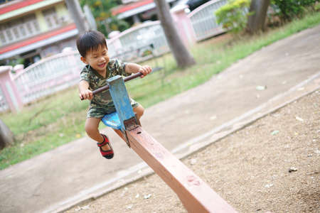 Asian boy about 2 year and 3 months in military suit playing seesaw and having fun with his mother at kid training playground for muscle developmentの写真素材