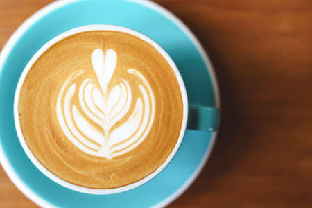 Cup of coffee with latte art pattern milk foam on wooden table