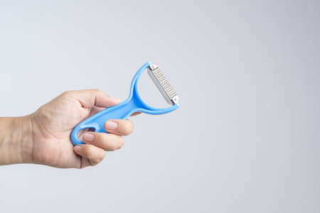 Hand holding plastic fruit peeler with blue handle on white background