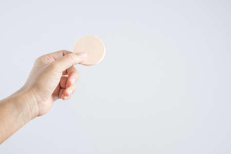 Hand holding round brown face sponge for cosmetic on white backgroundの写真素材
