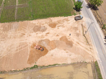Tractor leveling dirt floor and filling soil in flooded paddy field for new construction at Asian...