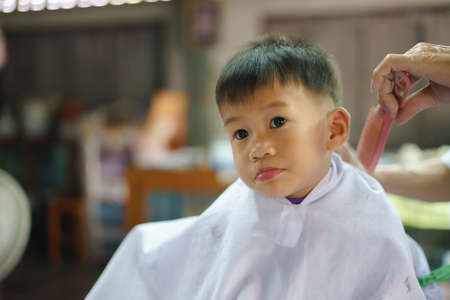 Asian boy about 2 year and 8 months getting haircut by professional barber at local shopの写真素材