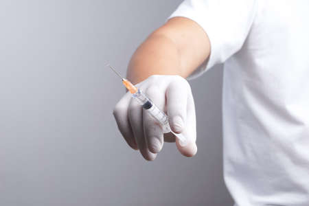 Hand wearing latex glove holding syringe with a medicine on white backgroundの写真素材