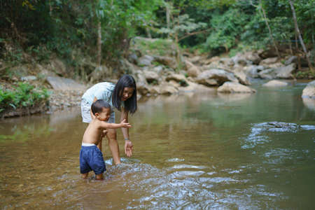 Asian mother in blue shirt with DIY chest pocket playing water with her son about 1 year and 9...