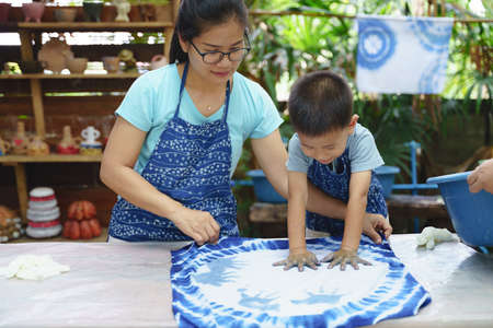 Asian mother and son playing art together by making northern thai blue dye fabric cloth textiles with hand printsの写真素材