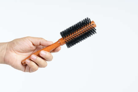 Hand holding hairdressing round brush comb with wooden handle on white backgroundの写真素材