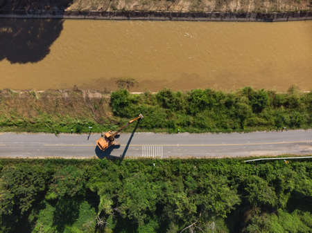 Excavator backhoe extracting soil and dirt from water canal at Asian countryside road