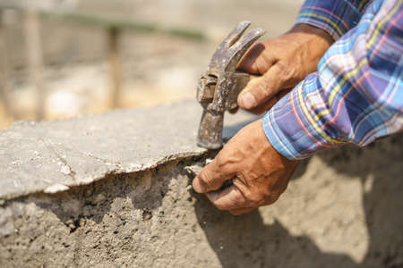 Worker labor hitting building concrete wall with hammer at house construction siteの写真素材