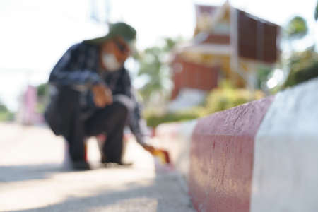 Asian worker painting red and white stripes on the edge of footpath road for no parking sign