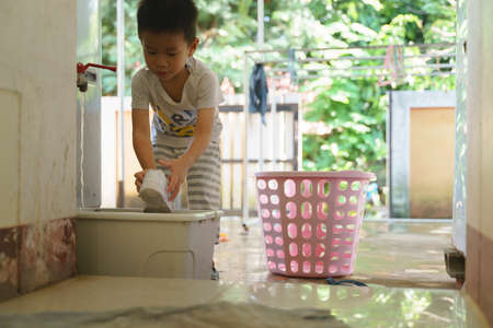 Asian boy help doing chores by washing shoes with brush and detergentの写真素材