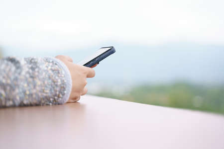 Woman hand with sweater addict and  keep using mobile phone while on the vacation in cold seasonの写真素材