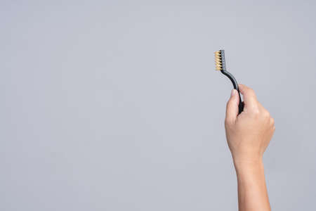 Hand holding small brass brush with plastic handle on white backgroundの写真素材