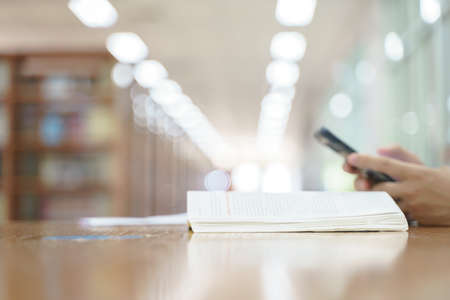 Thai student using mobile phone next to the book in public libraryの写真素材