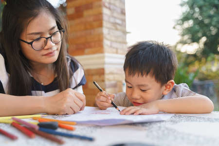 Asian boy drawing and painting homework picture by using color pencils with his mother