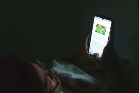 Chiangrai, Thailand, 15 October 2019, Thai woman upload and tagging keywords to Shutterstock application for selling picture online at night.のeditorial素材