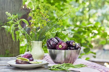 Ripe violet sweet pepper in metal plate and aromatic herbs in ceramic vase on the tableの写真素材
