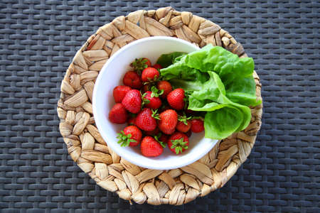 Strawberries and lettuce into a bowl on a wicker plate on a textural backgroundの写真素材
