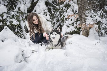 Beautiful girl plays with a dog in a snowy forest.の写真素材