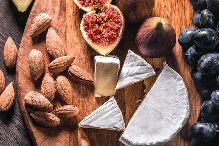 Cheese plate served with grapes, figs and nuts on a wooden background. Close - up.の写真素材
