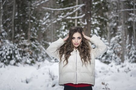 Young, beautiful girl, straightens her hair, standing in a snowy forest.